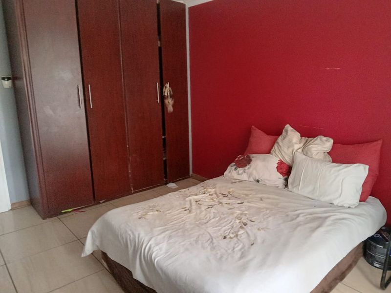 A bedroom featuring tiled flooring and a built-in wooden wardrobe, currently finished with a bold red accent wall.