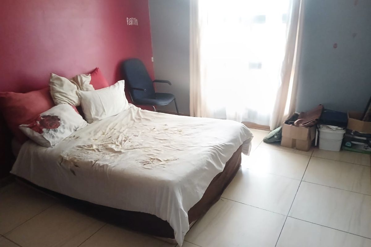A bedroom featuring tiled flooring and a large window, currently requiring cosmetic updates to the wall finishes.