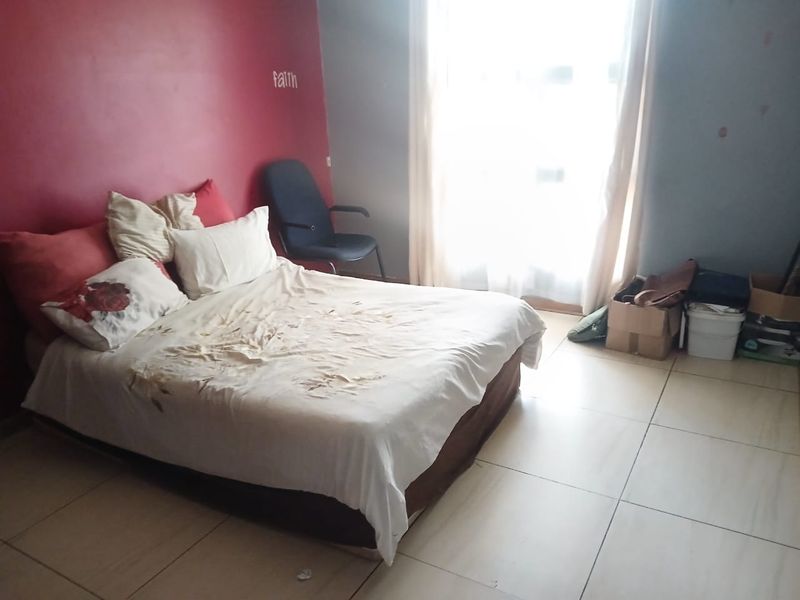 A bedroom featuring tiled flooring and a large window, currently requiring cosmetic updates to the wall finishes.