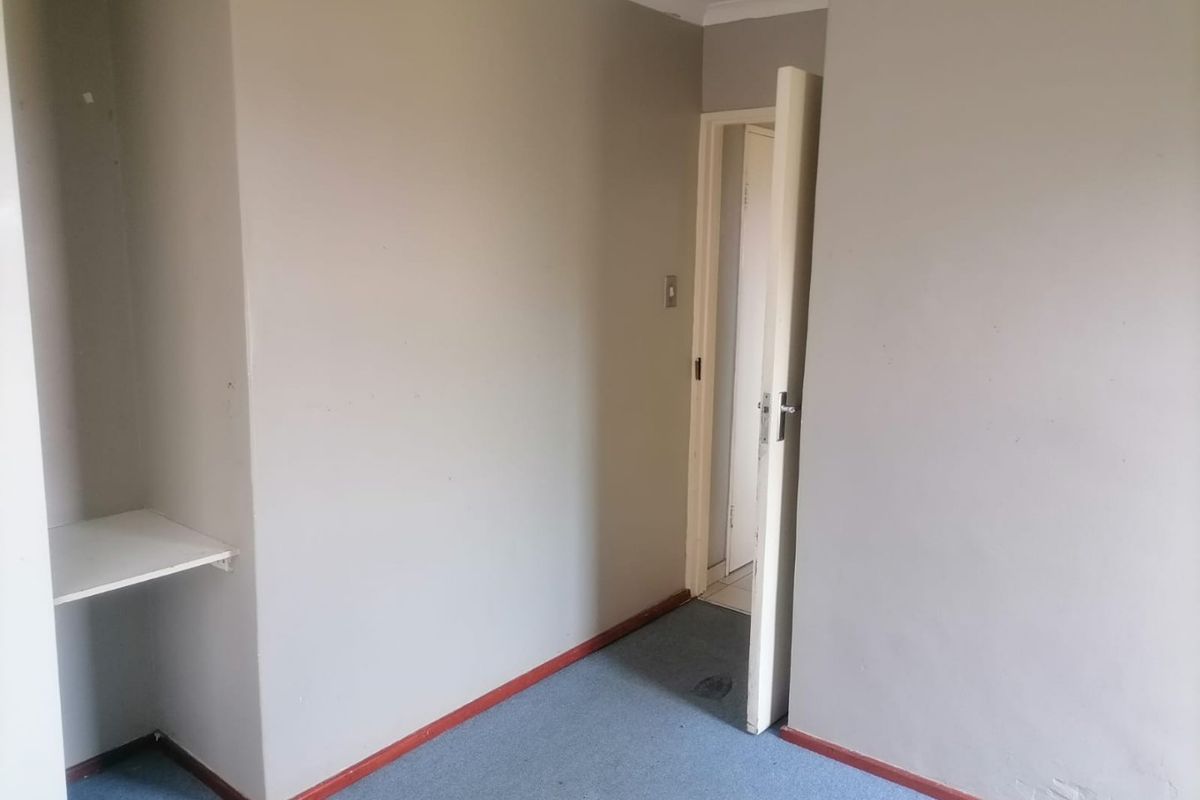 An empty bedroom featuring neutral walls, carpeted flooring, and built-in shelving, offering a blank canvas for potential interior design updates.