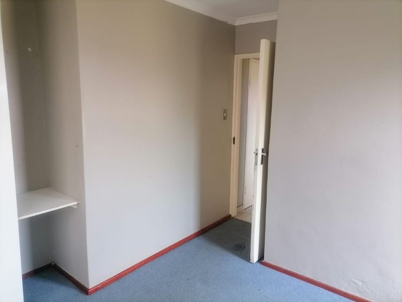 An empty bedroom featuring neutral walls, carpeted flooring, and built-in shelving, offering a blank canvas for potential interior design updates.