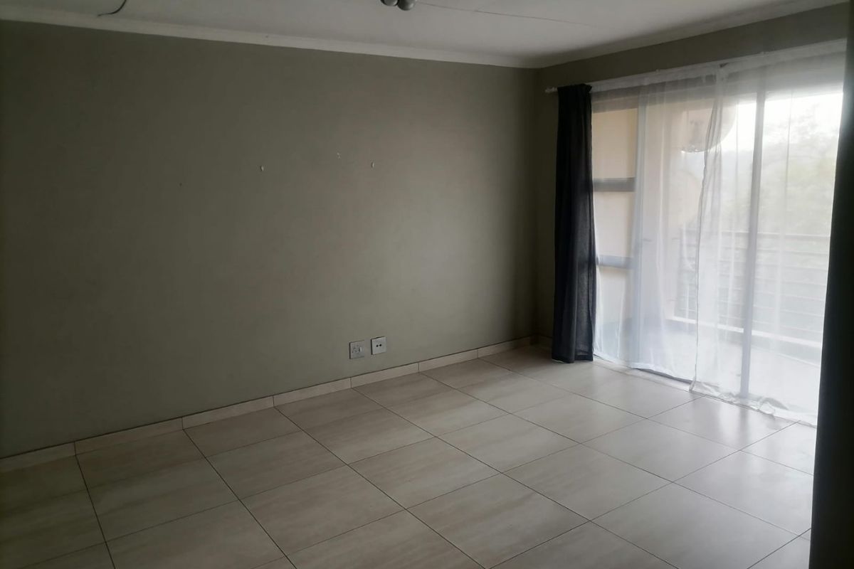 An empty living room featuring neutral tiled flooring, a sliding glass door leading to a balcony, and neutral wall finishes.
