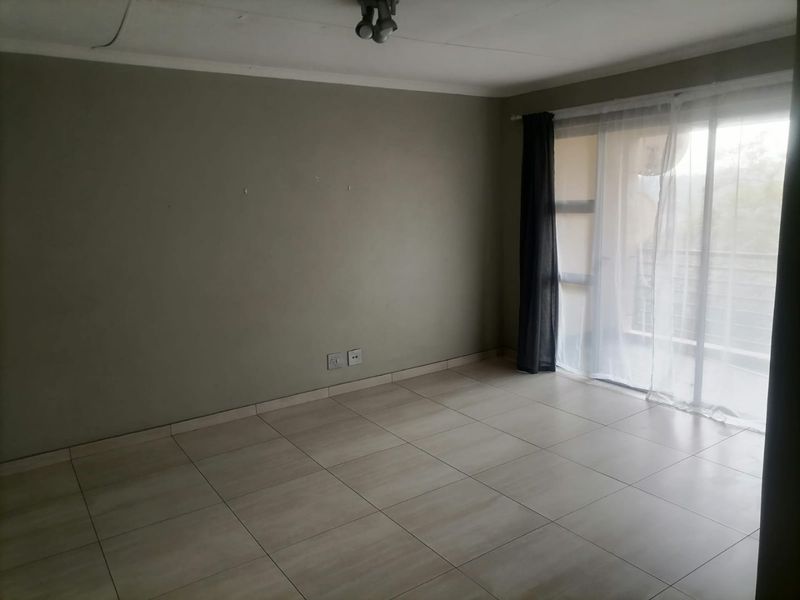 An empty living room featuring neutral tiled flooring, a sliding glass door leading to a balcony, and neutral wall finishes.