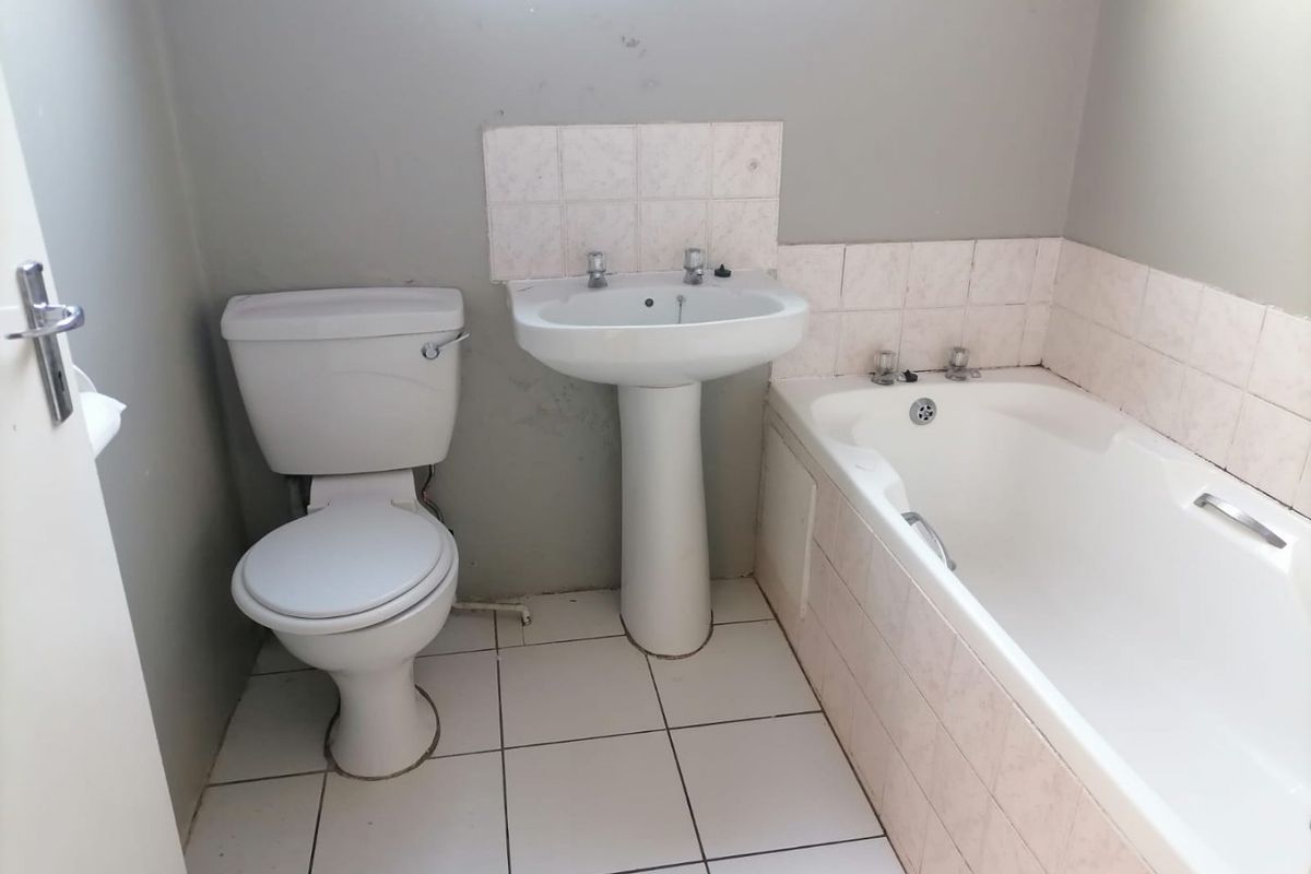 A functional bathroom featuring a pedestal basin, standard toilet, and a bathtub with tiled splashbacks and flooring, requiring cosmetic updates.