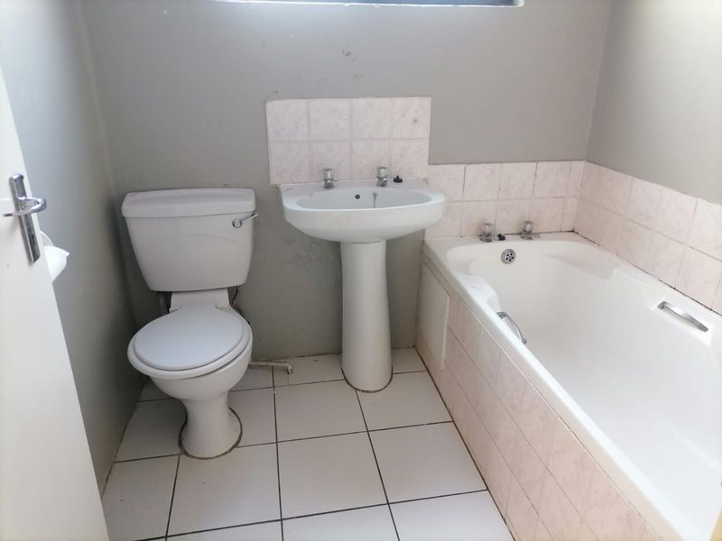 A functional bathroom featuring a pedestal basin, standard toilet, and a bathtub with tiled splashbacks and flooring, requiring cosmetic updates.