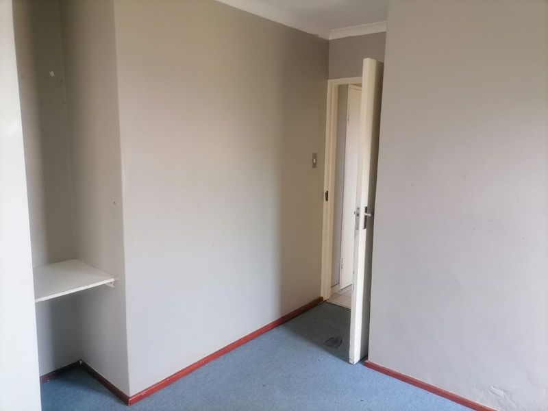An empty bedroom featuring carpeted flooring, built-in shelving, and neutral wall paint, providing a blank canvas for potential renovation or interior design updates.
