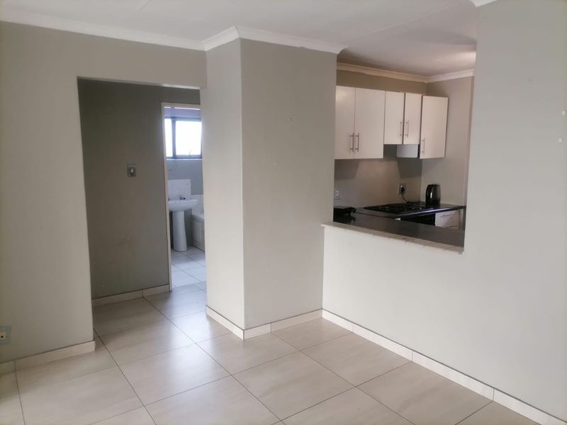 Open plan living area featuring tiled flooring, leading to a functional kitchen with built-in cabinetry and a separate bathroom with a pedestal basin.