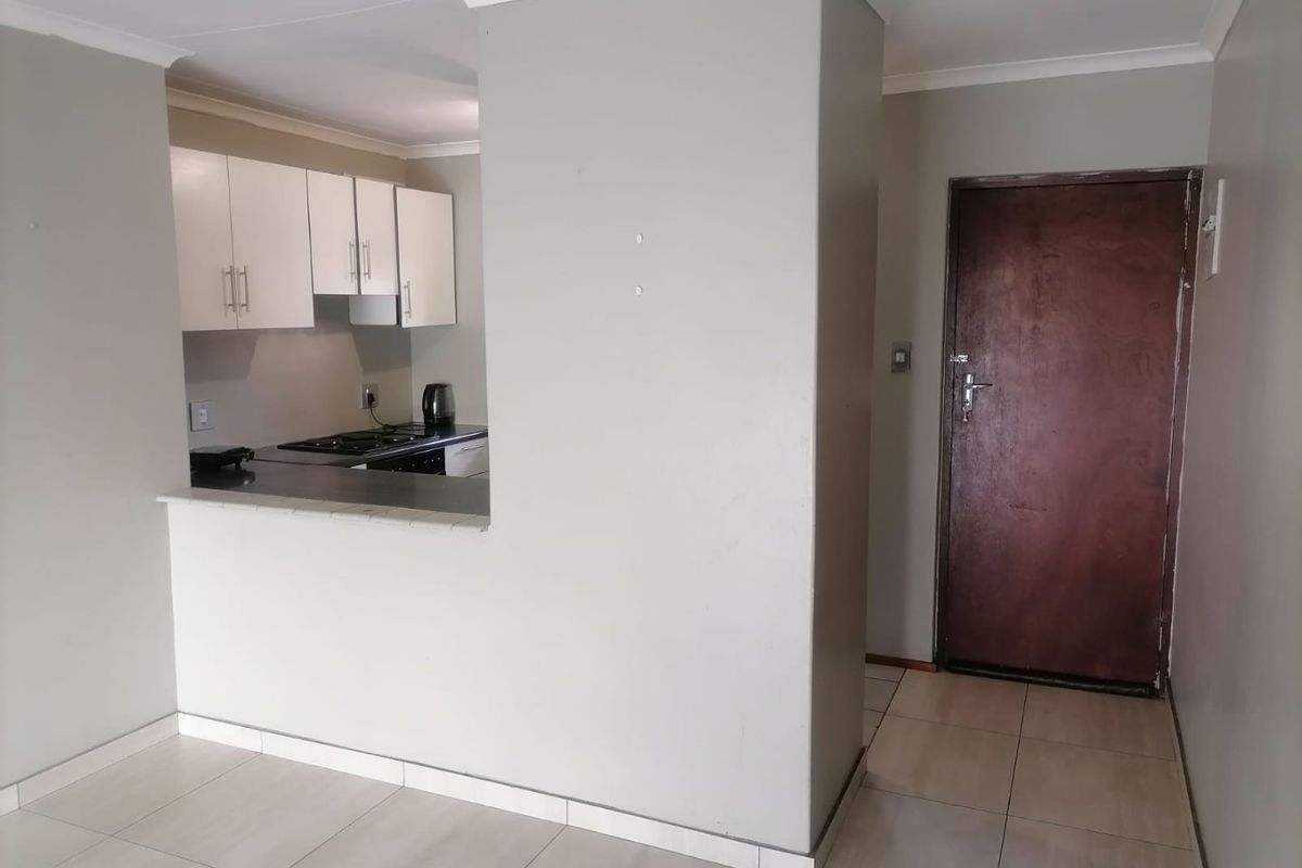 Open plan living area featuring tiled flooring and a compact kitchen with built-in cabinetry and hob, adjacent to the main entrance door.
