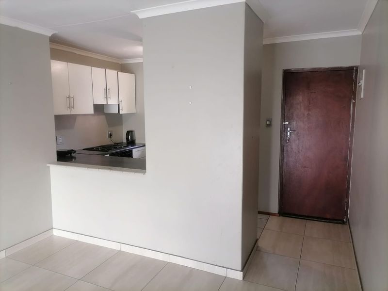 Open plan living area featuring tiled flooring and a compact kitchen with built-in cabinetry and hob, adjacent to the main entrance door.