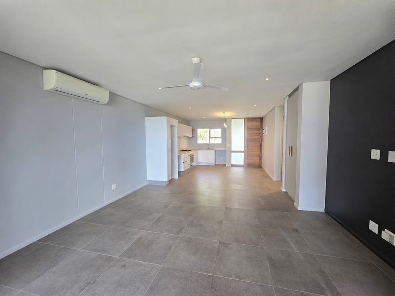 Spacious open-plan living area featuring large format floor tiles, air conditioning, a ceiling fan, and a modern kitchen with built-in appliances.