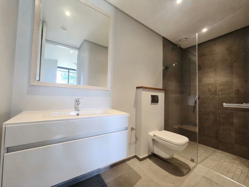 Modern bathroom featuring a wall-mounted vanity with integrated basin, wall-hung toilet with concealed cistern, and a spacious walk-in shower with glass screen.
