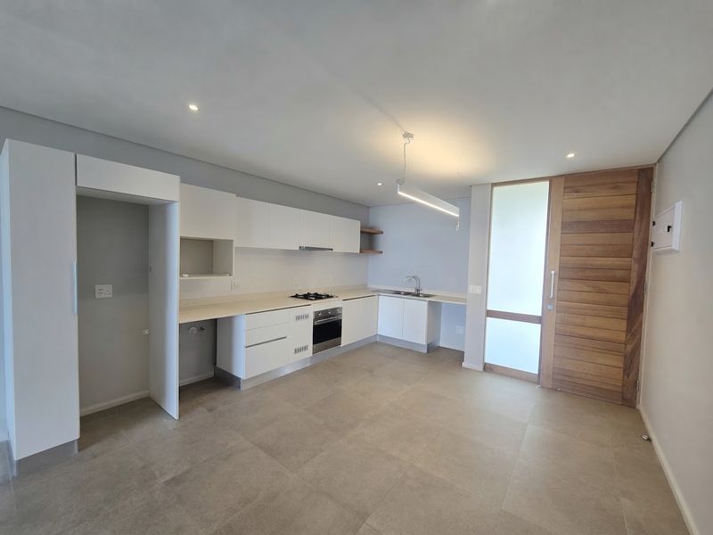 Modern kitchen featuring white cabinetry, built-in gas hob, oven, and tiled flooring, adjacent to a timber entrance door in an open-plan layout.