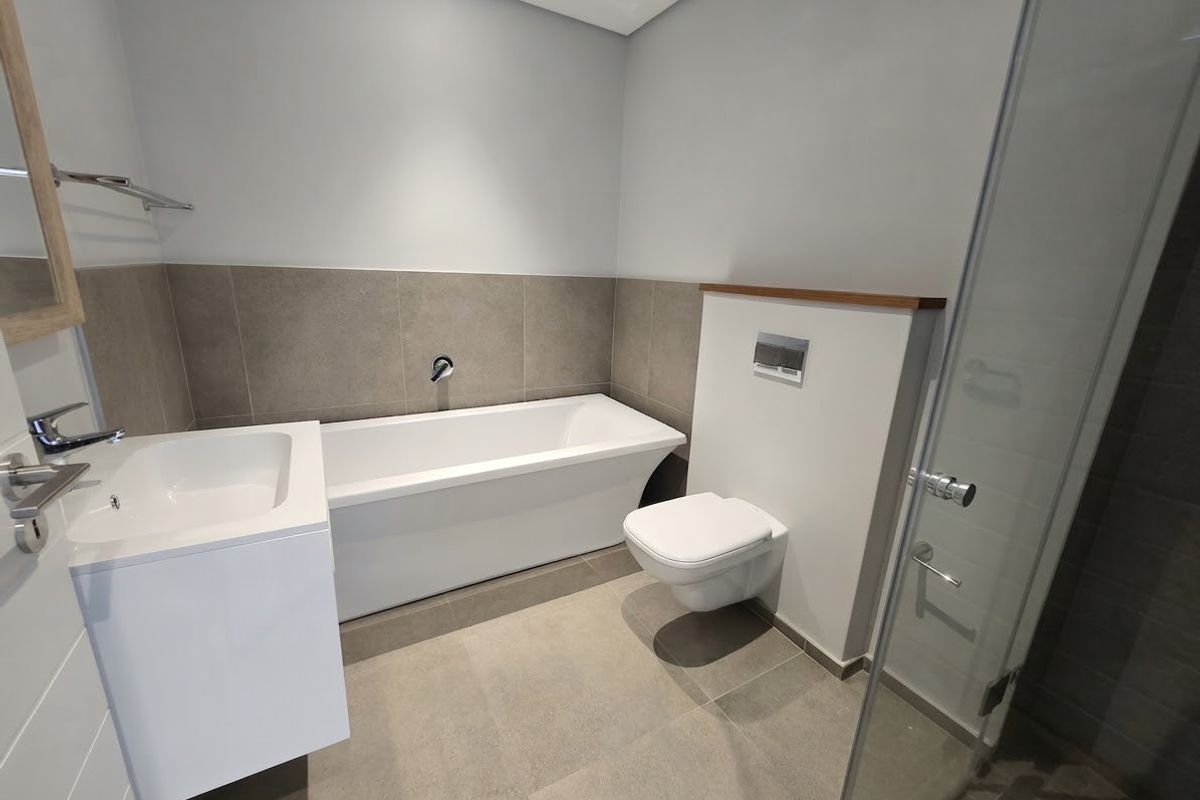 Modern bathroom featuring a sleek freestanding bathtub, wall-mounted toilet, vanity basin, and a glass-enclosed shower with contemporary neutral tiling.