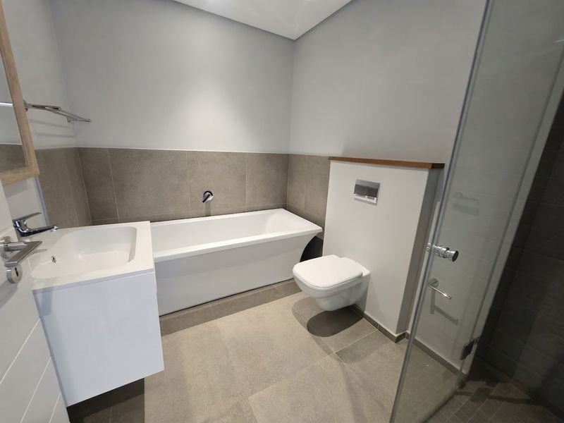 Modern bathroom featuring a sleek freestanding bathtub, wall-mounted toilet, vanity basin, and a glass-enclosed shower with contemporary neutral tiling.