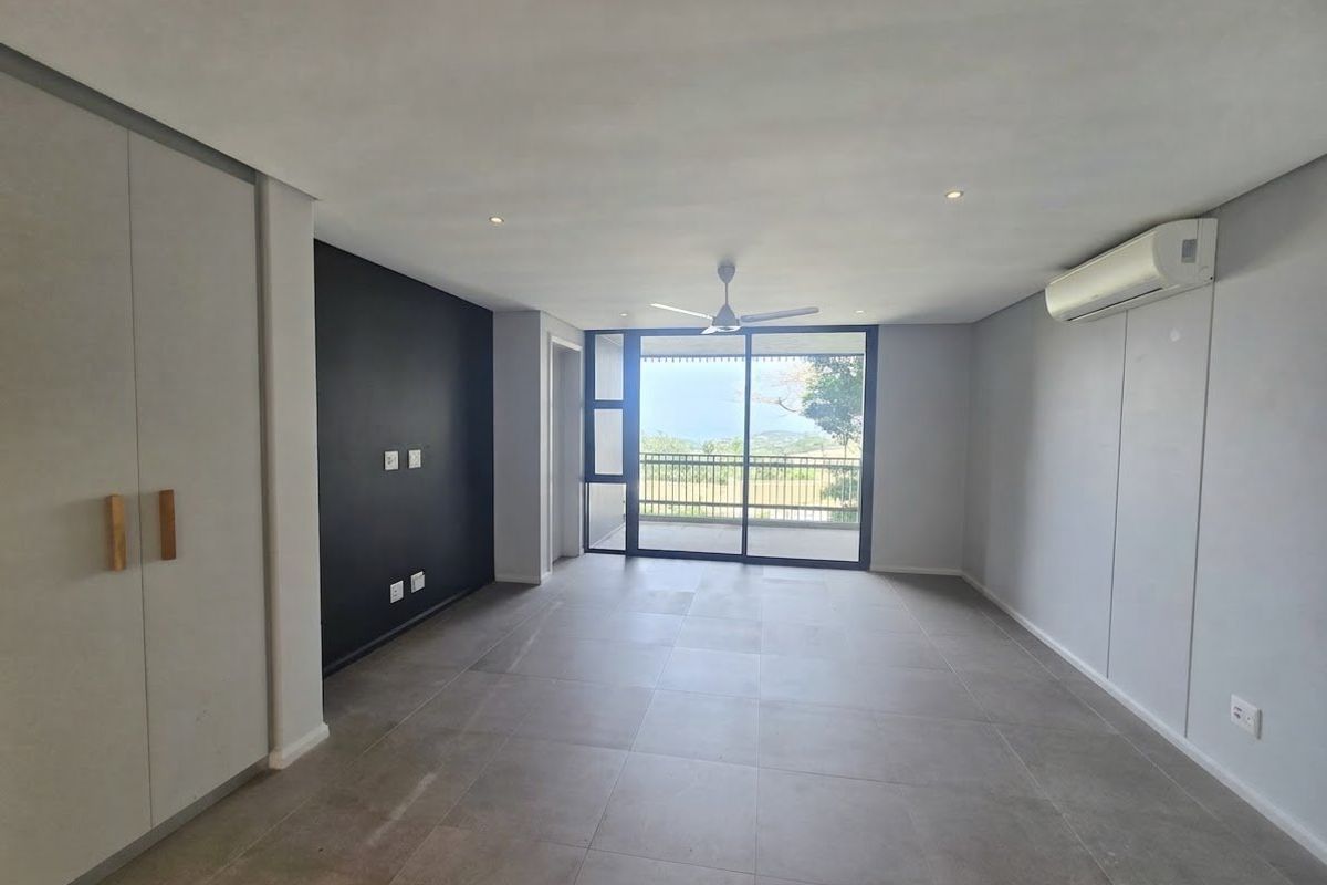 A bright, modern, and empty living room featuring large format floor tiles, a ceiling fan, air conditioning, and sliding doors leading to a balcony.