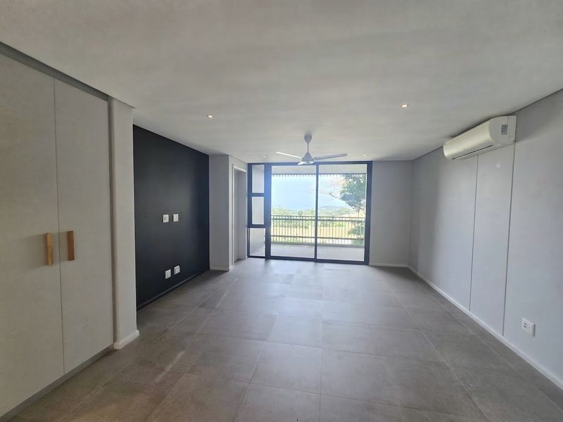 A bright, modern, and empty living room featuring large format floor tiles, a ceiling fan, air conditioning, and sliding doors leading to a balcony.