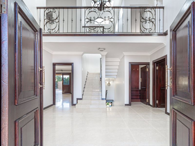 Spacious double-volume entrance hall featuring tiled flooring, a grand staircase, and an elegant wrought iron balustrade overlooking the foyer.