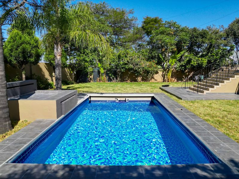 A well-maintained outdoor pool area featuring a tiled surround, built-in bench seating, and a wrought iron staircase leading to the upper level.