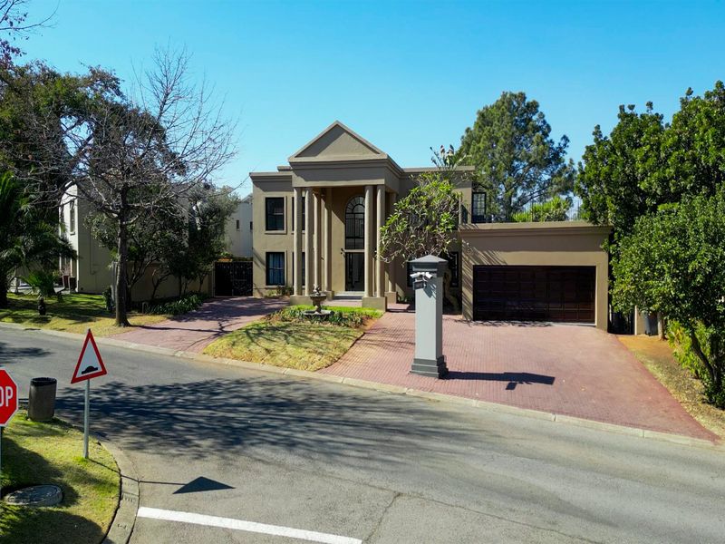 A stately double-story residence featuring a grand portico entrance, paved driveway, and integrated double garage, set within a well-maintained suburban landscape.