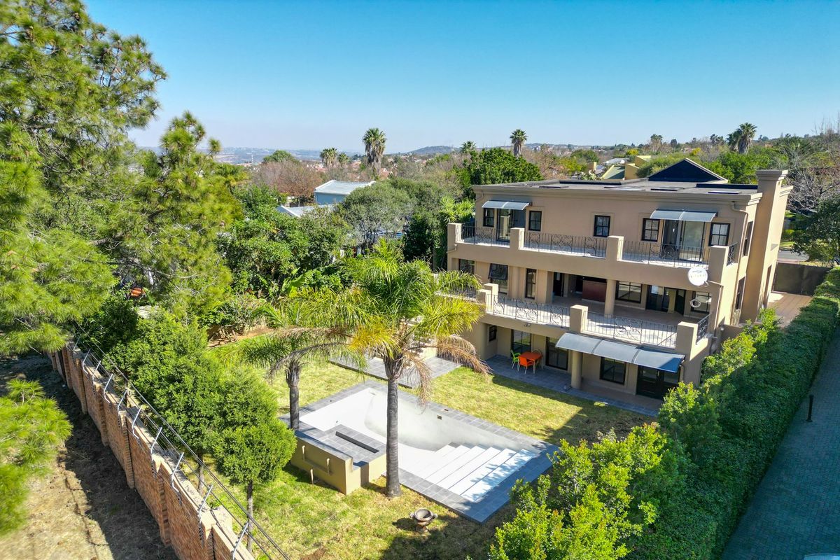 Aerial view of a multi-story residential property featuring a swimming pool, landscaped garden, and spacious balconies with wrought iron railings.