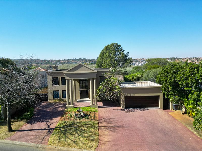Aerial view of a stately residence featuring a paved driveway, double garage, and a prominent portico entrance with classic columns.