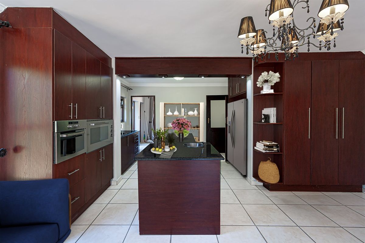 A well-appointed kitchen featuring dark wood cabinetry, a central island with a granite countertop, built-in appliances, and tiled flooring.