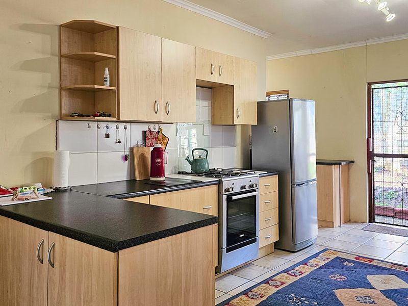 Functional kitchen featuring light wood-finish cabinetry, dark laminate countertops, tiled backsplash, and a built-in gas hob and oven, with direct access to the exterior.