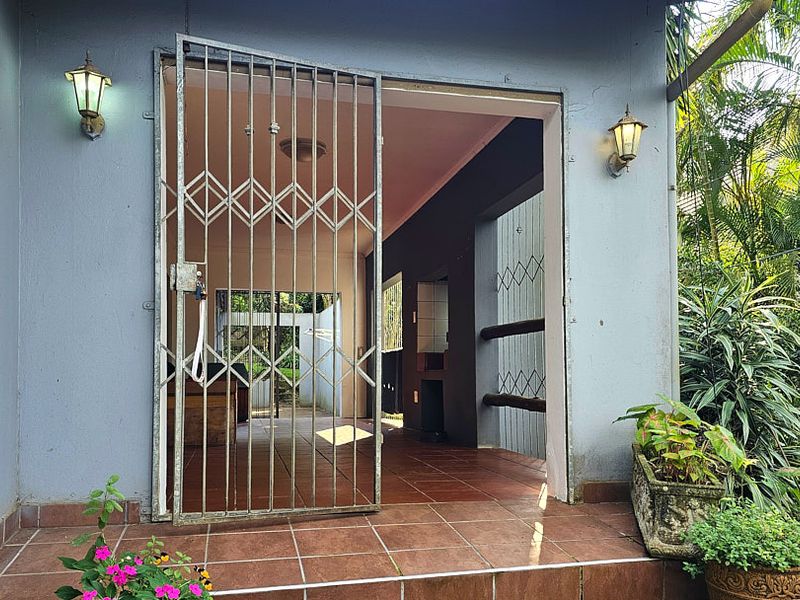 A covered patio area featuring tiled flooring, a security gate, and a built-in braai, providing a functional outdoor entertainment space.