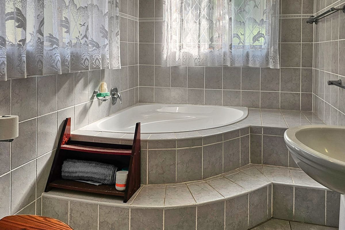 A functional bathroom featuring a corner bathtub with tiled surround, pedestal basin, and neutral ceramic wall tiling.