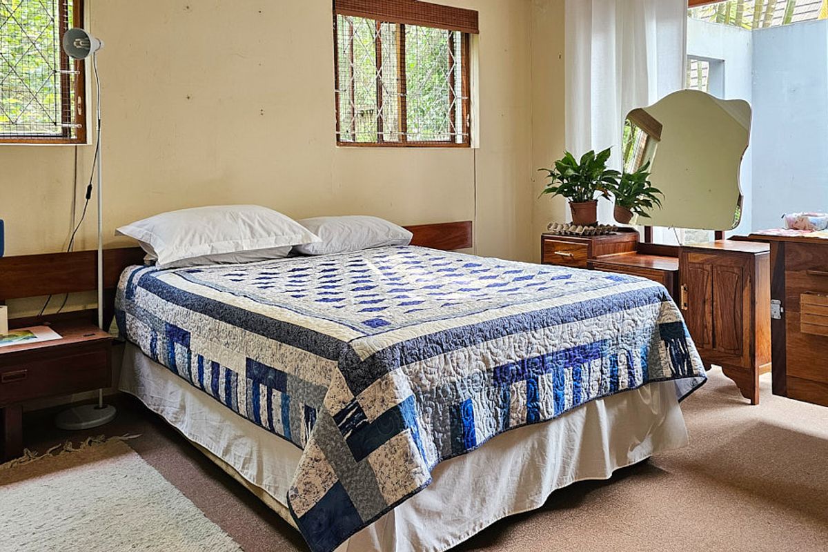A bedroom featuring a built-in wooden headboard, carpeted flooring, and windows fitted with security bars, offering a functional space with potential for cosmetic updates.
