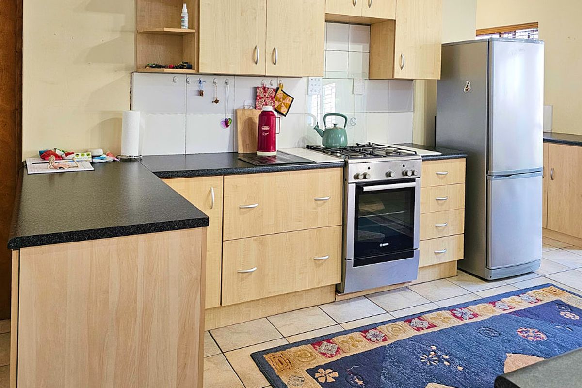 Functional kitchen featuring light wood-finish cabinetry, dark laminate countertops, a gas hob, built-in oven, and tiled flooring.