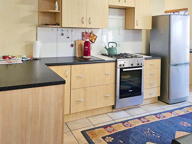 Functional kitchen featuring light wood-finish cabinetry, dark laminate countertops, a gas hob, built-in oven, and tiled flooring.