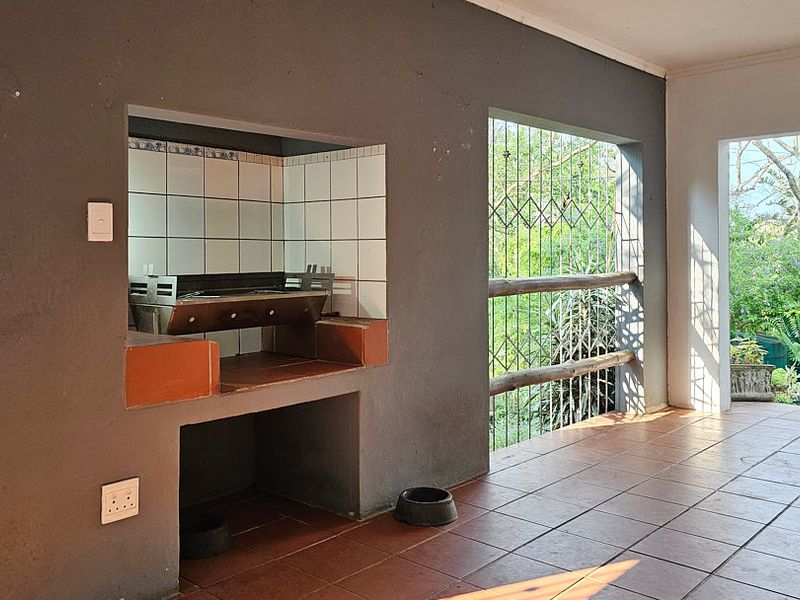 Covered patio area featuring a built-in braai, tiled flooring, and security gates, offering a functional outdoor entertainment space.