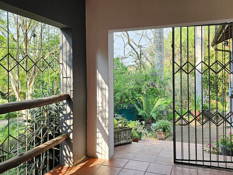 A covered patio area featuring tiled flooring, security gates, and direct access to the garden, providing a functional outdoor living space.
