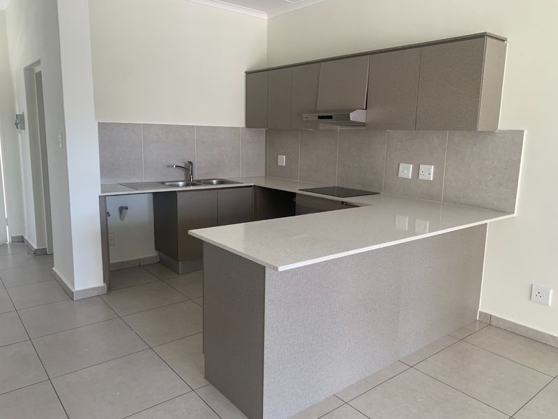 Modern kitchen featuring neutral-toned built-in cabinetry, stone countertops, an electric hob with extractor, and tiled flooring in a clean, open-plan layout.