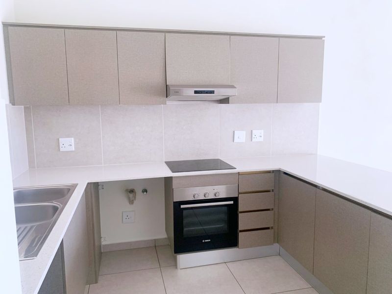 Modern kitchen featuring neutral cabinetry, stone countertops, integrated oven and hob, and tiled backsplash. Space is ready for appliance installation.