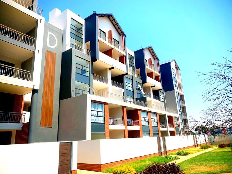 A modern multi-story apartment building featuring contemporary architectural design, private balconies with metal railings, and a well-maintained landscaped garden area.