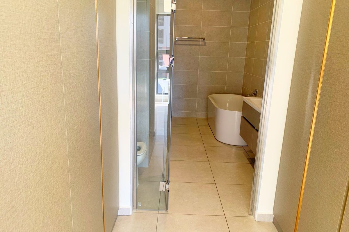 A modern, clean bathroom featuring a freestanding bathtub, wall-mounted vanity, and a glass-enclosed shower area with neutral floor-to-ceiling tiling.