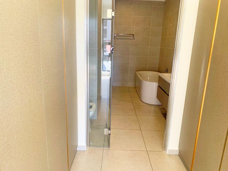 A modern, clean bathroom featuring a freestanding bathtub, wall-mounted vanity, and a glass-enclosed shower area with neutral floor-to-ceiling tiling.