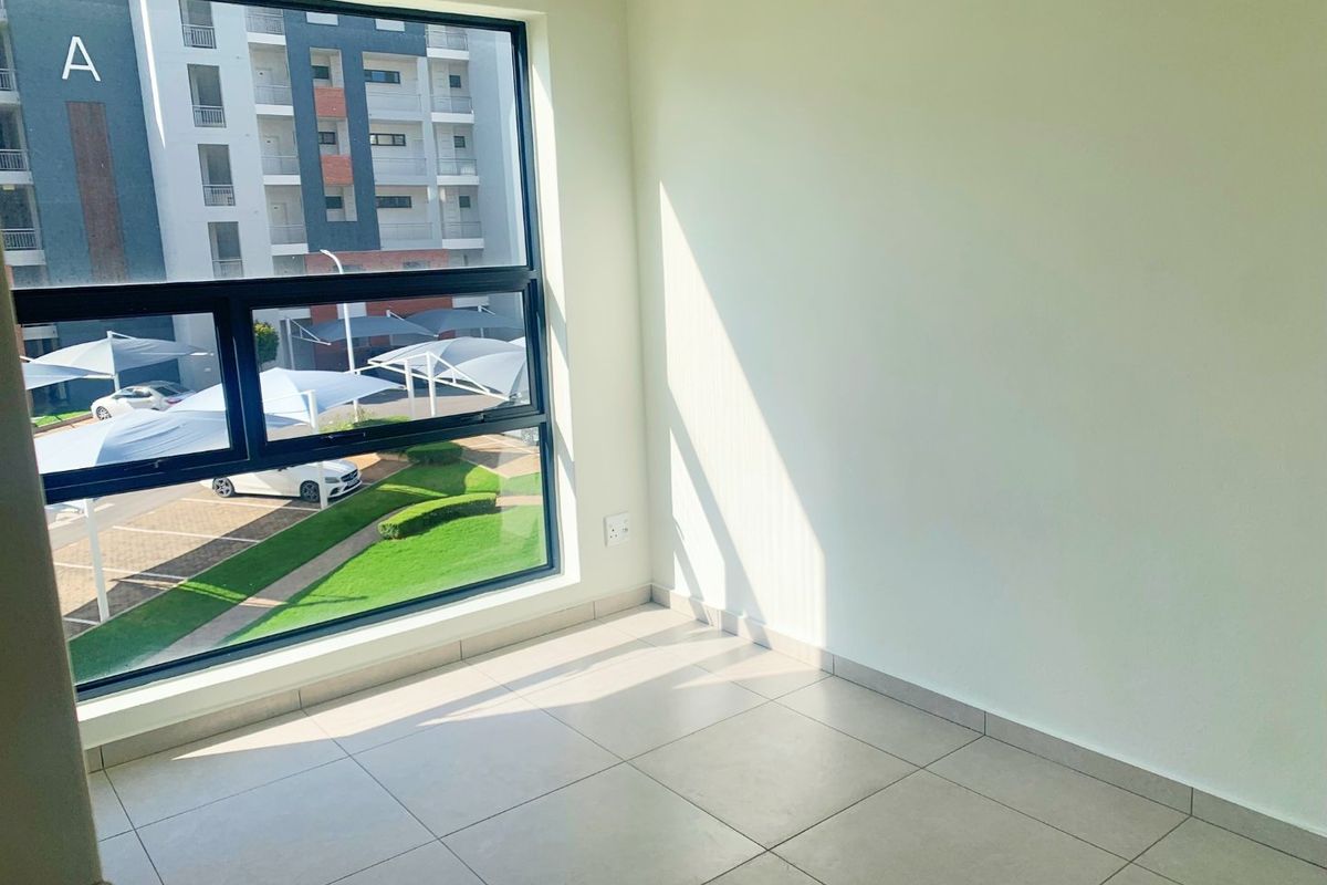 A bright, empty bedroom featuring large aluminium-framed windows, neutral tiled flooring, and clean white walls, offering a modern and versatile living space.