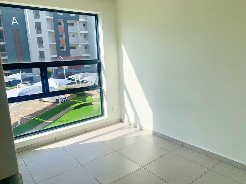 A bright, empty bedroom featuring large aluminium-framed windows, neutral tiled flooring, and clean white walls, offering a modern and versatile living space.