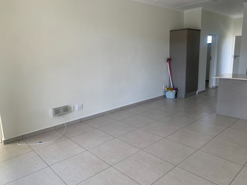 An open-plan living area featuring neutral tiled flooring, a built-in cupboard, and a kitchen island, offering a clean and versatile space.