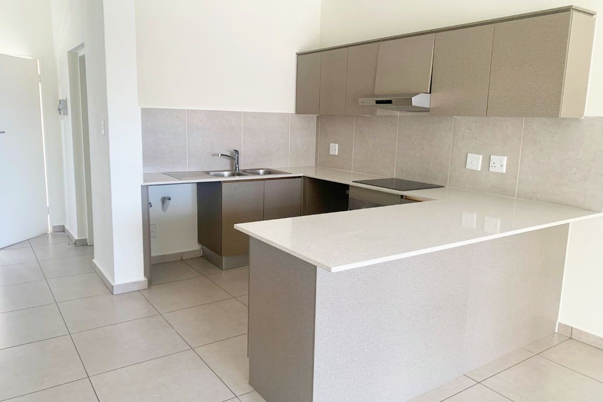 Modern kitchen featuring neutral-toned built-in cabinetry, stone countertops, an electric hob with extractor fan, and tiled flooring in an open-plan layout.