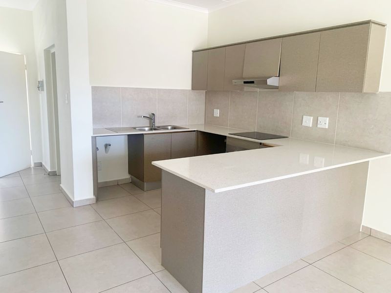 Modern kitchen featuring neutral-toned built-in cabinetry, stone countertops, an electric hob with extractor fan, and tiled flooring in an open-plan layout.