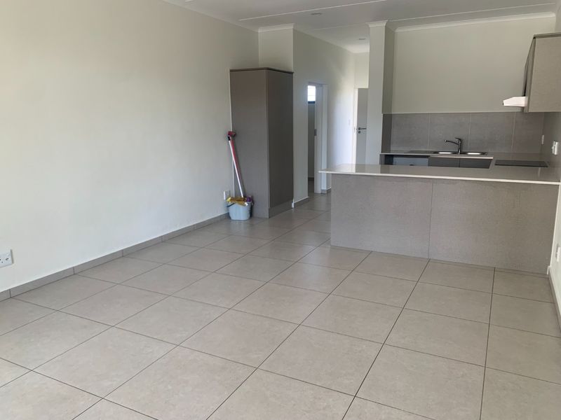 An open-plan living and kitchen area featuring neutral tiled flooring, modern cabinetry, and a functional kitchen island with integrated sink and extractor fan.
