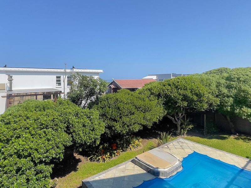 An elevated view of a private swimming pool with a pool cover, surrounded by a paved deck and established garden greenery.