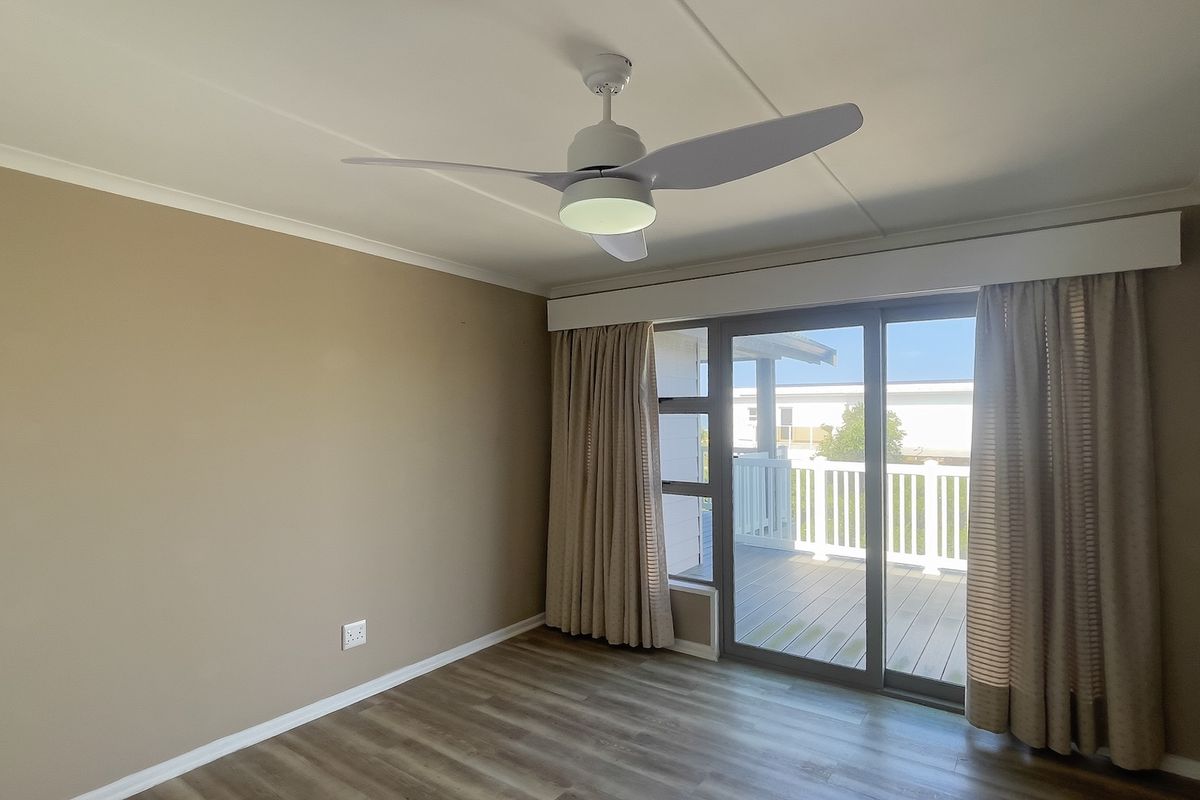 A bright, empty bedroom featuring modern laminate flooring, a ceiling fan, and sliding glass doors that open onto an outdoor deck.