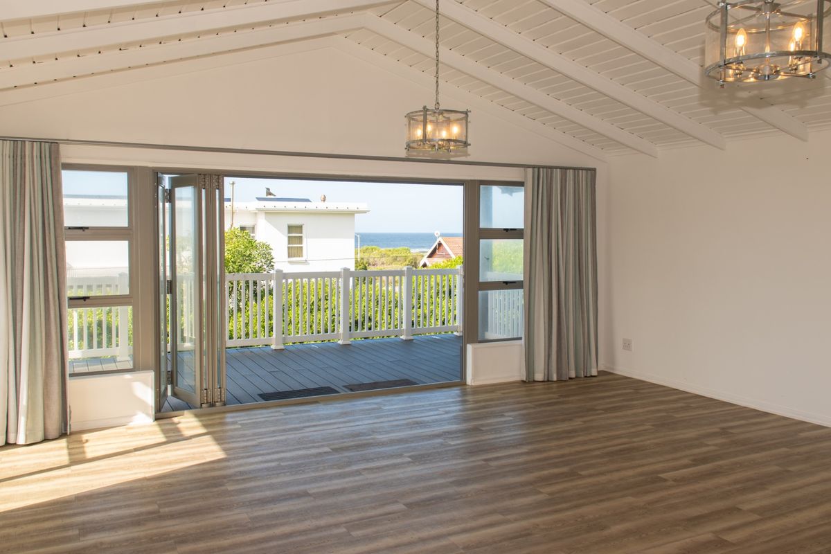 Spacious living area featuring vaulted ceilings with exposed beams, modern laminate flooring, and large bi-fold doors opening onto a deck with ocean views.