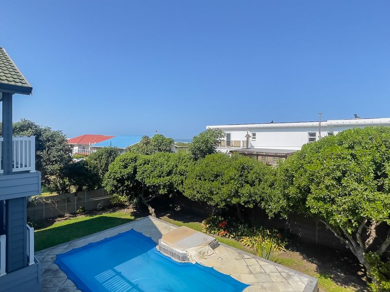 An elevated view of a private swimming pool with a cover, set within a landscaped garden area featuring mature trees and a balcony view.