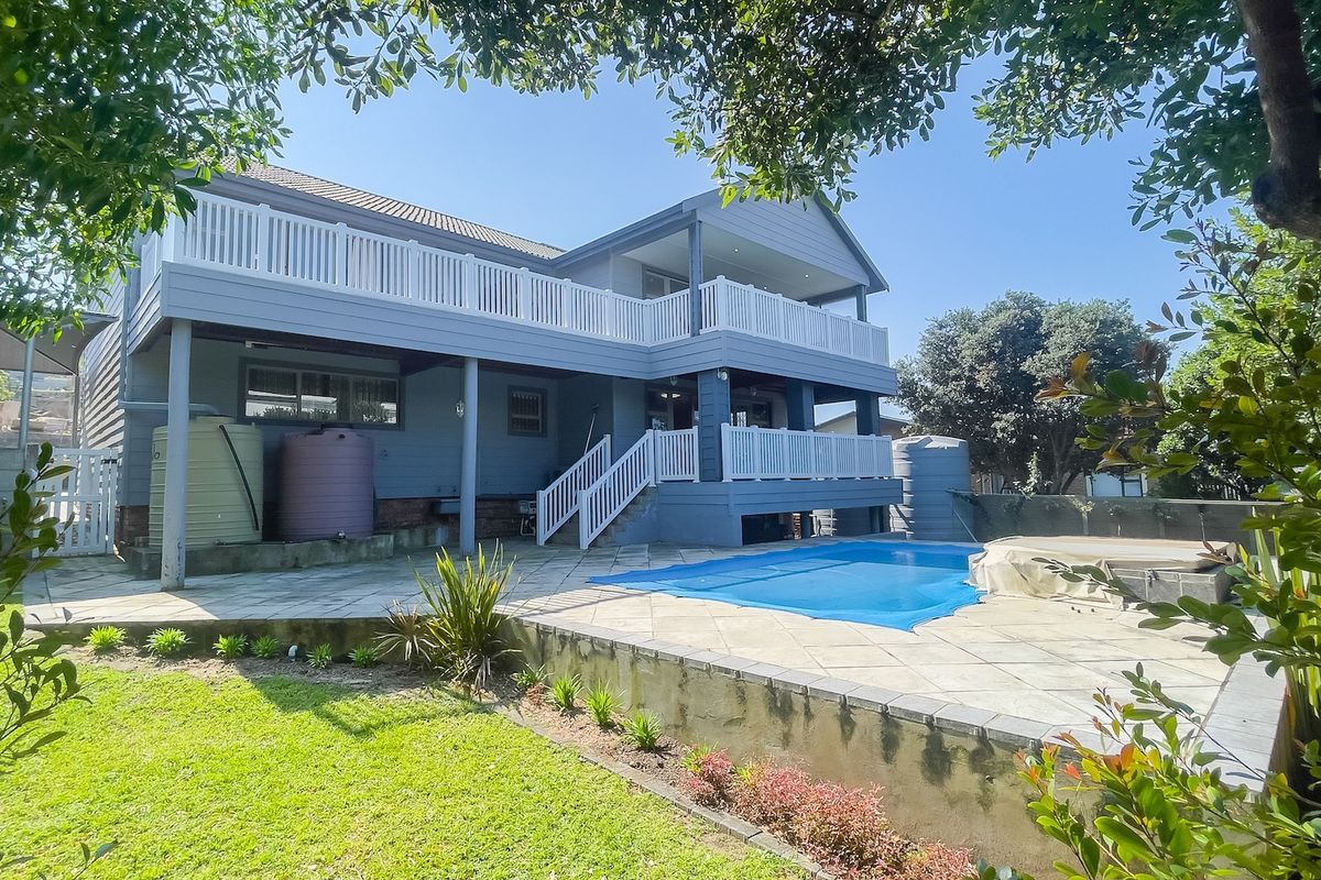 Rear exterior view featuring a swimming pool, paved patio area, and a multi-level deck with white balustrades overlooking the garden.